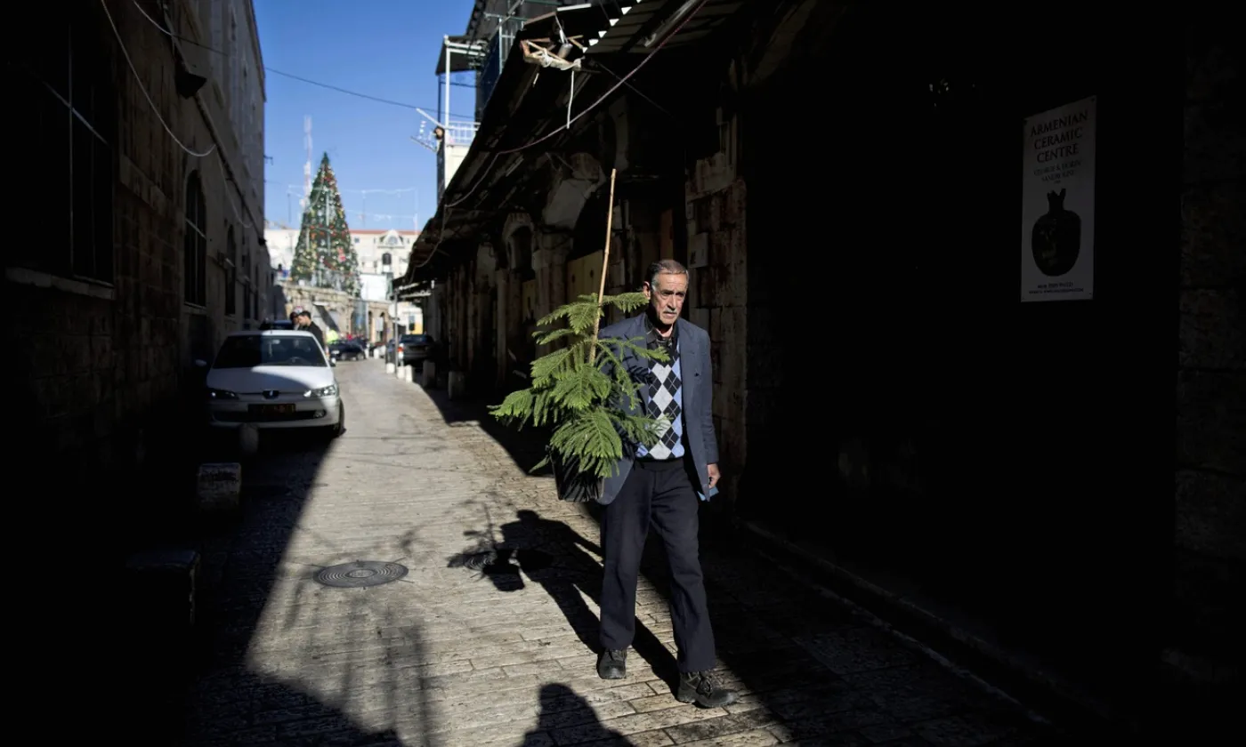 Un Palestinien portant un sapin de Noël dans une rue pavée de la vieille-ville de Jérusalem. Keystone/ Abir Sultan